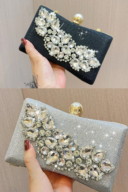 Black and silver clutch with crystal embellishments held by a hand against a beige background